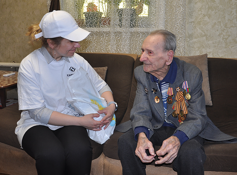 Главный специалист отдела по связи с общественностью «ЕвроХим-БМУ» Татьяна Мирошникова передаёт подарок ветерану Василию Акимову 