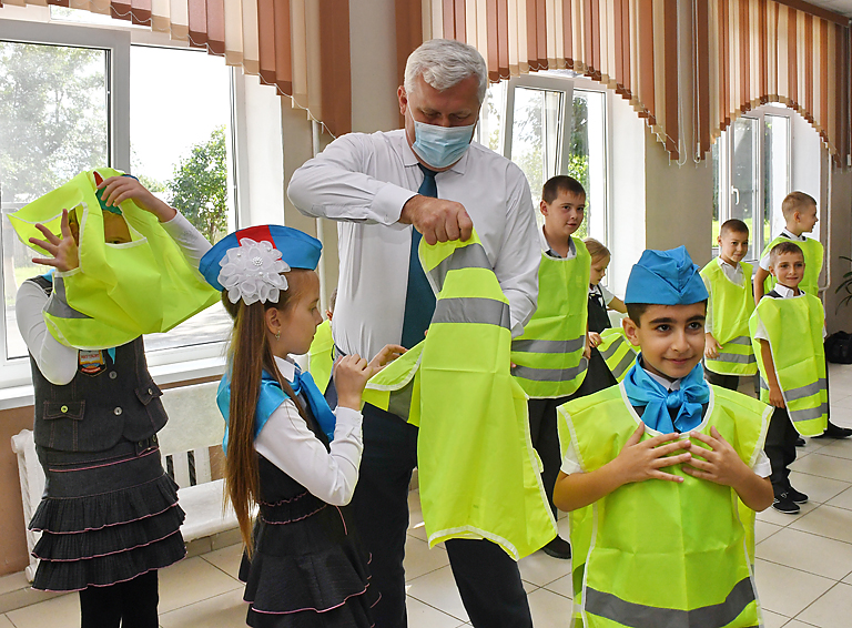 Глава района Александр Шаповалов помогает школьнице правильно надеть жилет и напоминает о необходимости носить его в тёмное время суток